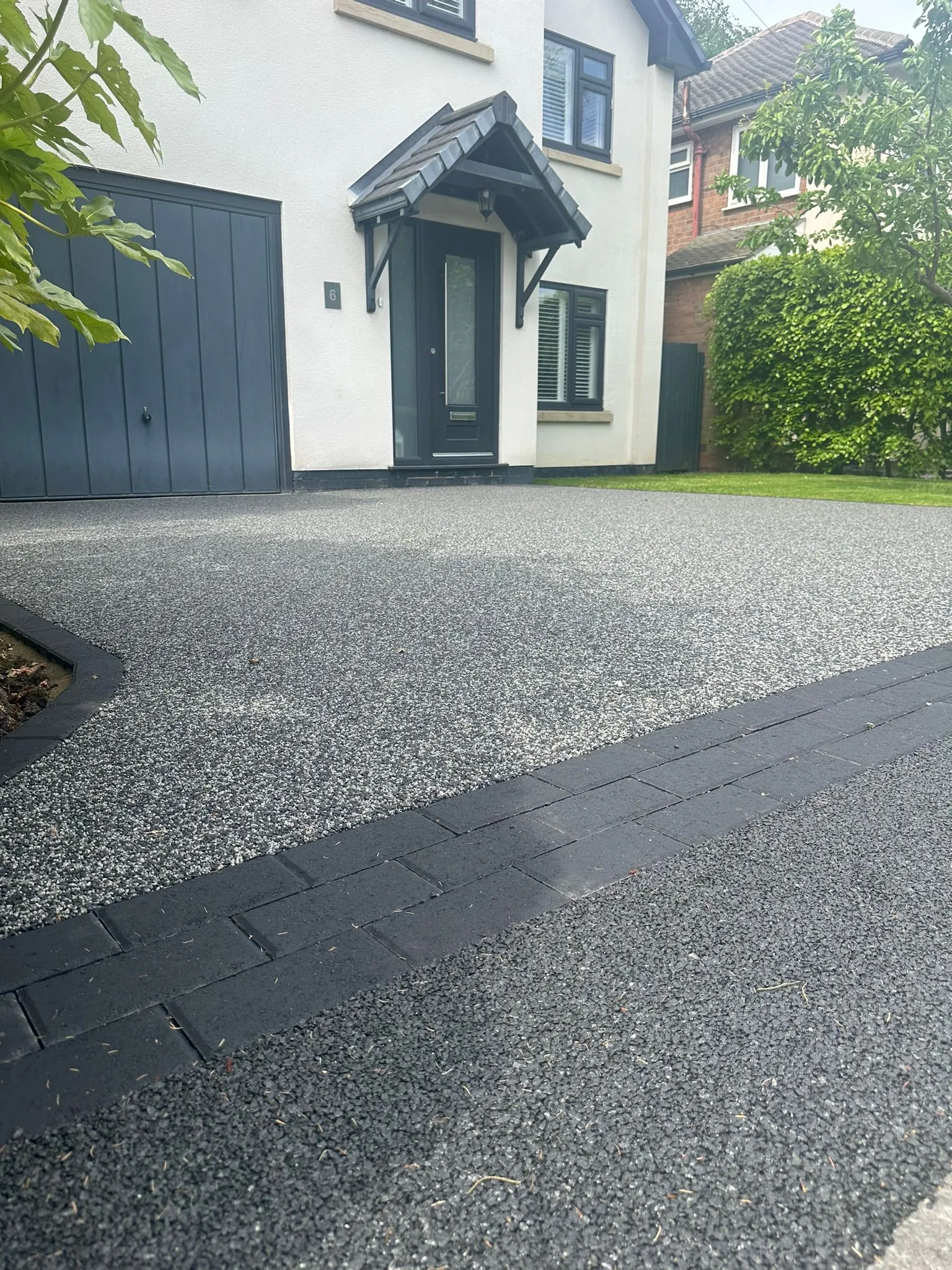 Charcoal resin drive at white rendered home with porch
