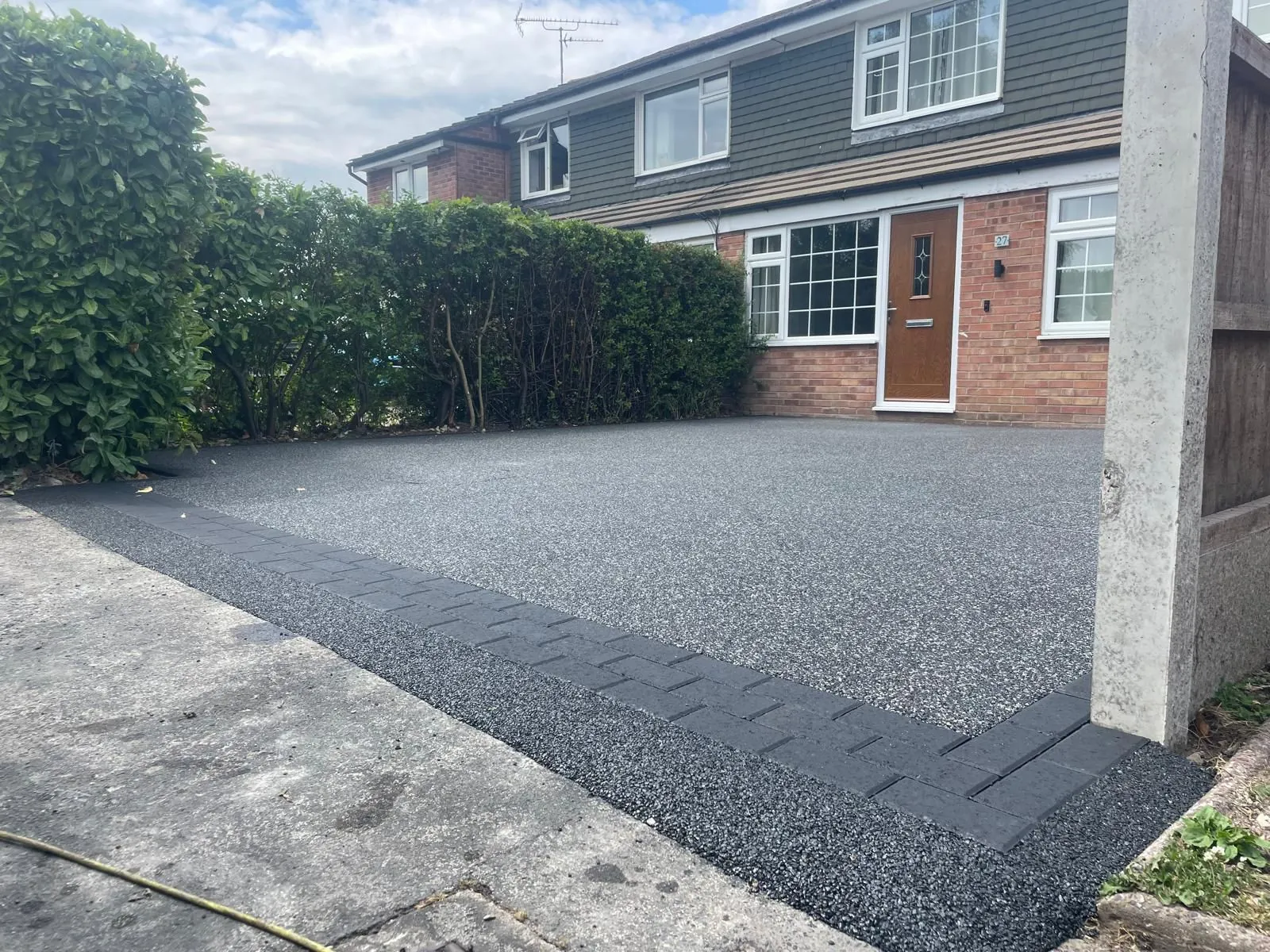 Charcoal resin driveway at modern semi with hedge border