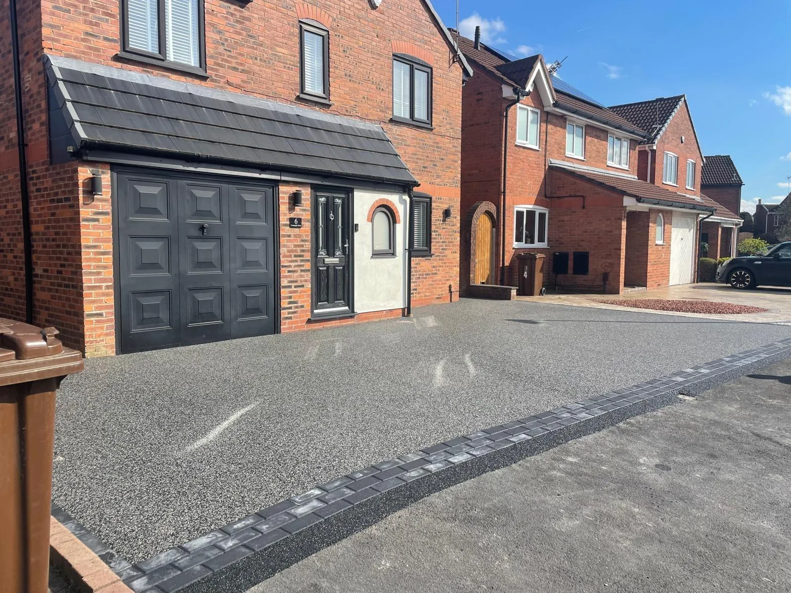 Silver resin driveway with block border at a new-build home with black garage, Manchester